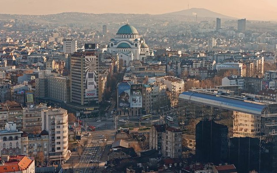 Aerial view of Belgrade at golden hour with the white Church of Saint Sava and its green domes above the city