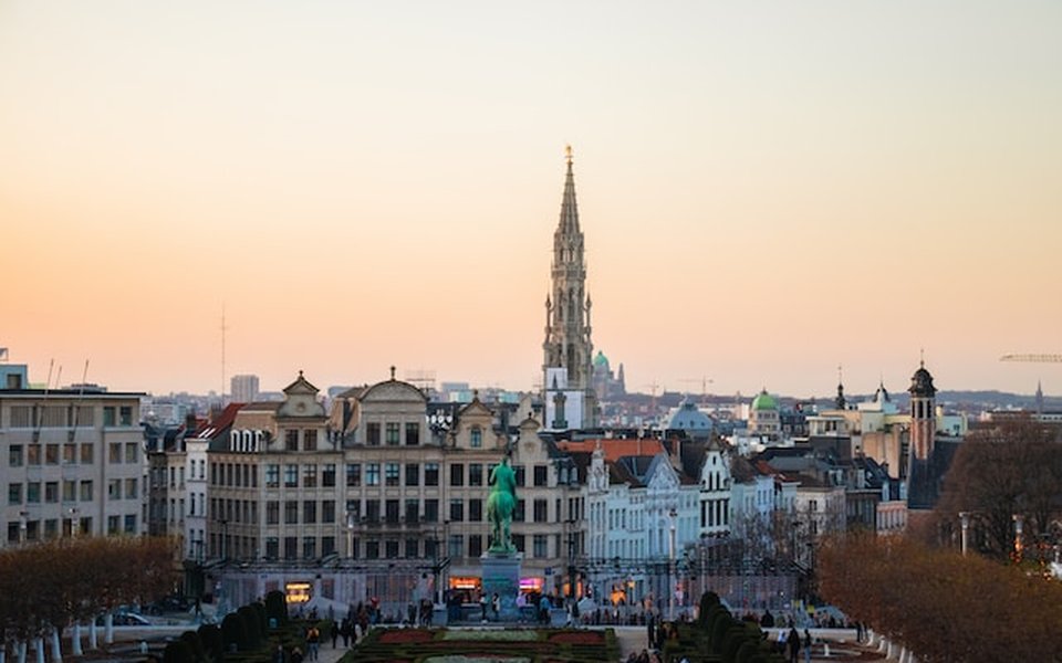 Elevated view of Brussels at sunset with the Town Hall Gothic spire above historic rooftops and the Mont des Arts gardens