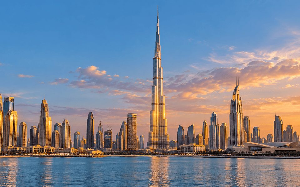 Dubai skyline at sunset with the Burj Khalifa towering over surrounding skyscrapers and calm water