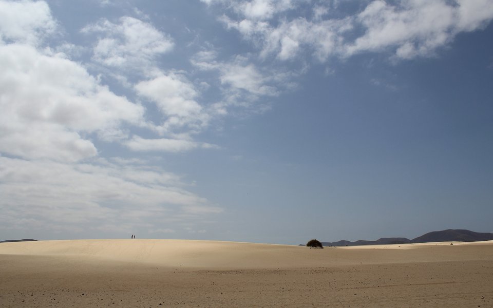 Pale sand dunes and distant volcanic hills under a bright blue sky in Fuerteventura