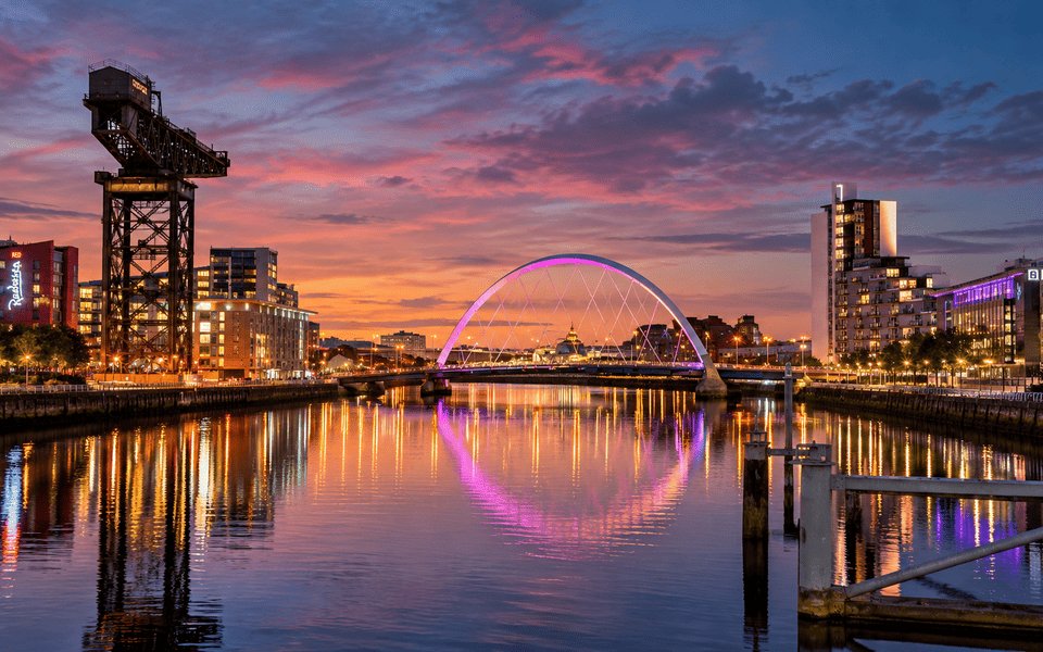 Dusk view of the River Clyde in Glasgow with the illuminated Clyde Arc bridge and historic Finnieston Crane against an orange and pink sunset