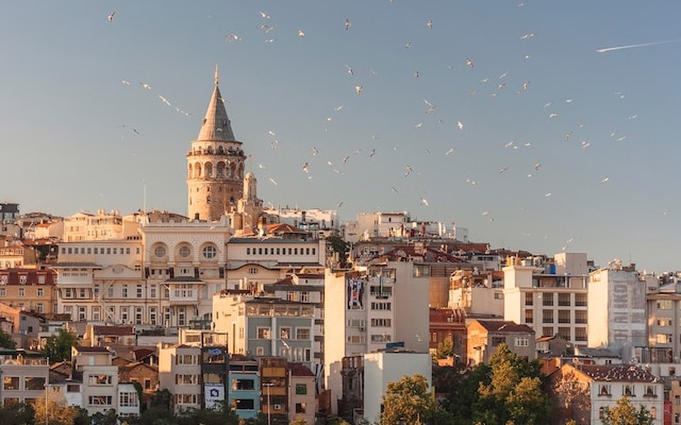 Galata Tower above the Istanbul skyline at golden hour with birds in flight