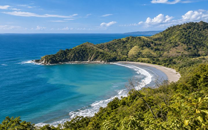 Elevated view of a crescent tropical bay with turquoise water and forested hills near Liberia, Costa Rica