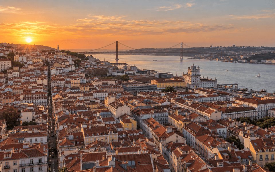 Aerial view of Lisbon with terracotta rooftops and the 25 de Abril Bridge at sunset