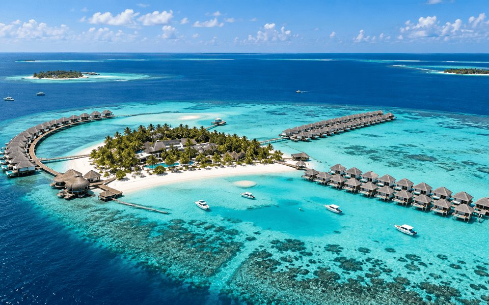 Aerial view of a Maldives resort island with overwater bungalows in a turquoise lagoon
