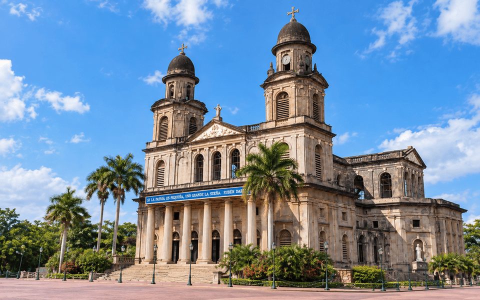 Old Cathedral of Managua with twin domed towers and palm trees on a sunny plaza