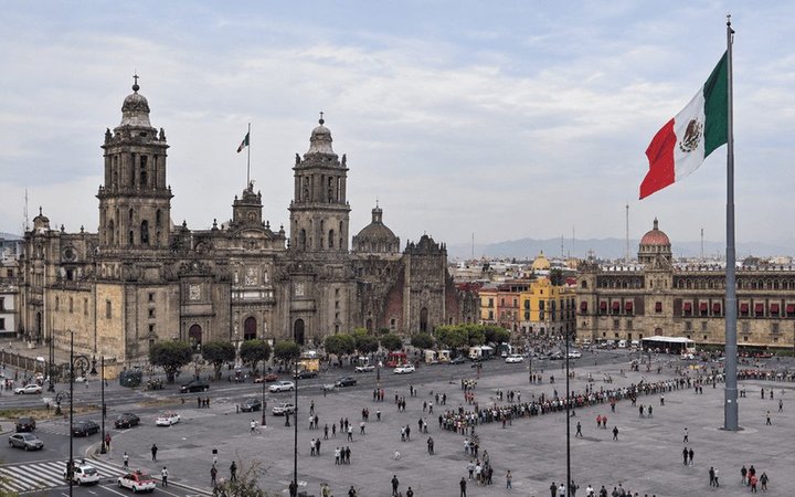 Mexico City Zócalo with the Metropolitan Cathedral, National Palace and a large Mexican flag under an overcast sky