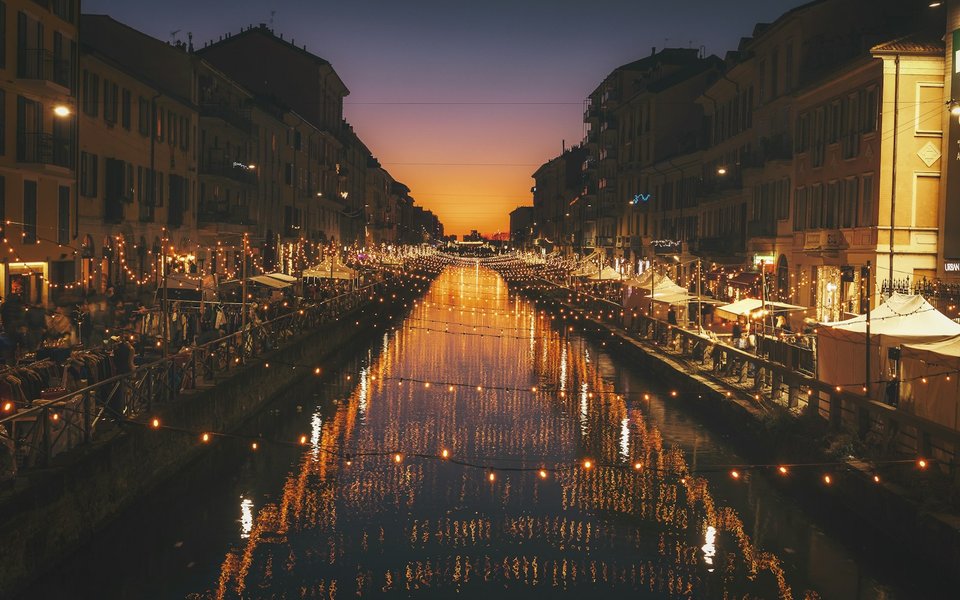 Sunset over the Naviglio Grande canal in Milan with string lights reflecting on the water