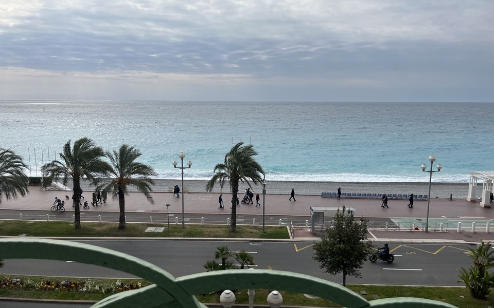 Promenade des Anglais in Nice with blue chairs, palm trees and the Mediterranean under a cloudy sky
