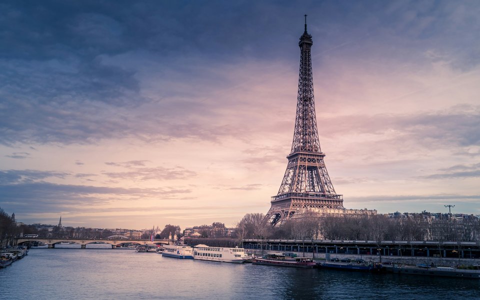The Eiffel Tower beside the Seine at twilight with riverboats moored along the bank