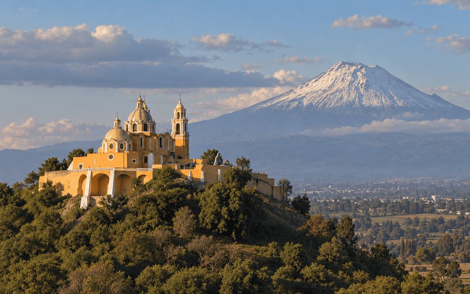 Yellow church of Nuestra Señora de los Remedios on the Cholula pyramid with snow-capped Popocatépetl beyond Puebla