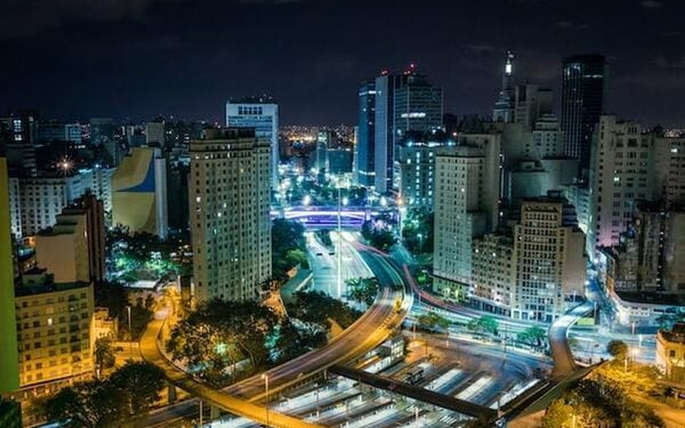 Night view of São Paulo with dense high-rises and light trails on a curving multi-lane highway