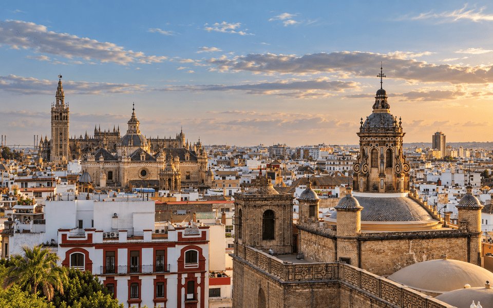 Golden-hour view of Seville with the Cathedral, Giralda and Iglesia del Salvador above terracotta rooftops