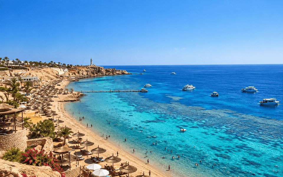 High-angle view of a Sharm El Sheikh Red Sea bay with turquoise water, thatched umbrellas and boats