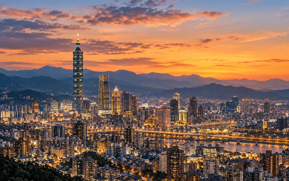Taipei skyline at sunset with Taipei 101 glowing above the city and mountains along the horizon