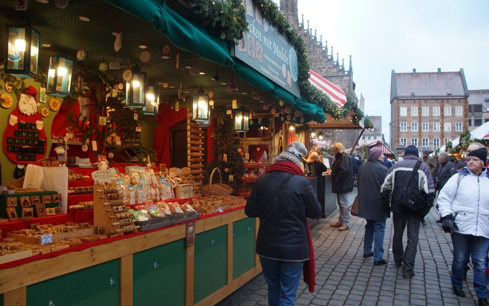 Traditional wooden Christmas market stall selling carved baking molds at the Nuremberg Christkindlesmarkt with a Gothic church spire beyond