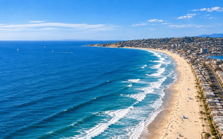 Sunlit San Diego coastline with a wide sandy beach, blue lifeguard towers and waves rolling toward shore