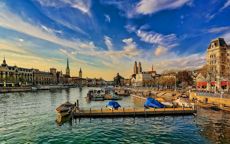 Boats on the Limmat River in Zurich with the Grossmünster twin towers and Fraumünster spire under a blue sky